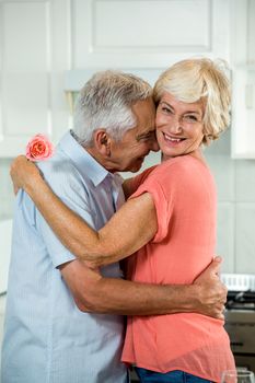 Romantic retired couple with rose while standing in kitchen