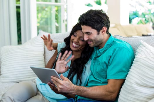 Couple waving hands while using digital tablet for video chat at home