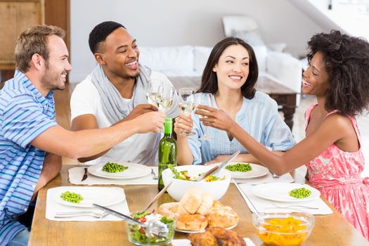 Friends toasting wine glasses while having a meal at dining table