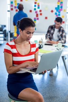 Young woman using laptop while colleagues working in the background