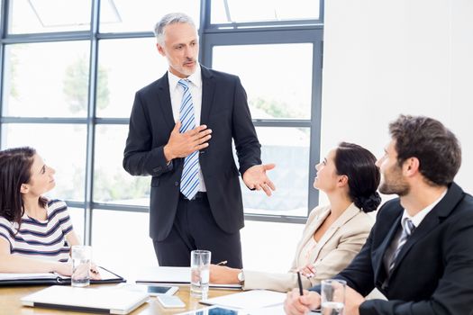 A businessman is standing in front of his colleagues and talking at work