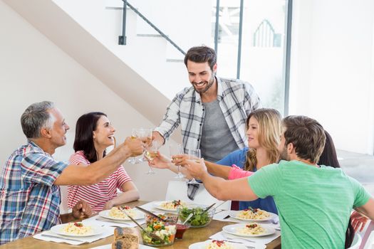 Friends toasting wine glasses while having a meal at dining table