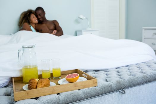 Romantic couple cuddling with breakfast tray on bed in bedroom
