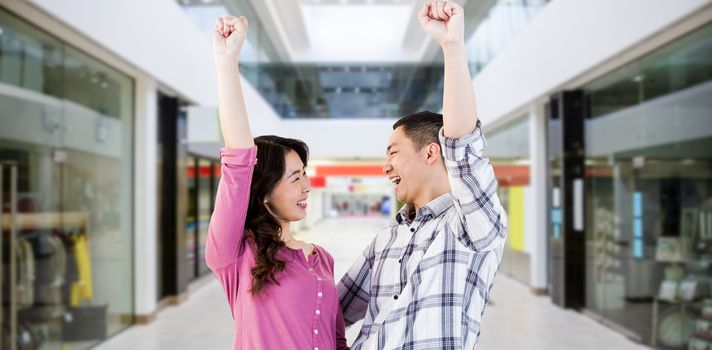 Cheerful young couple with hands raised against interior of modern shopping mall