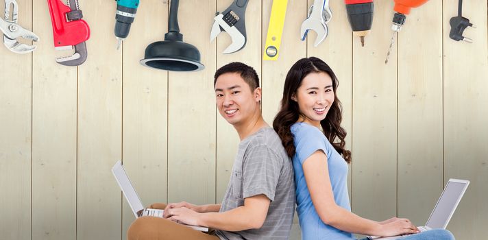 Portrait of young happy couple using laptop while sitting against diy tools on wooden background