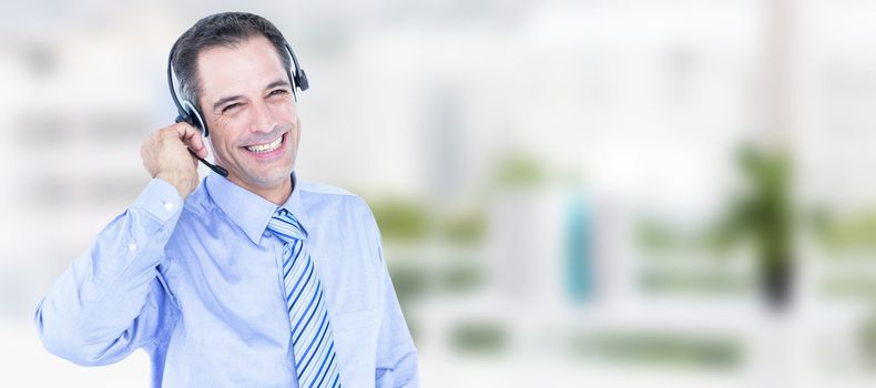 Smiling businessman using headset against office