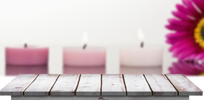 Wooden floor against lighted candles and a pink gerbera