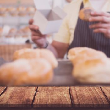 Wooden table against worker in apron holding box and bread