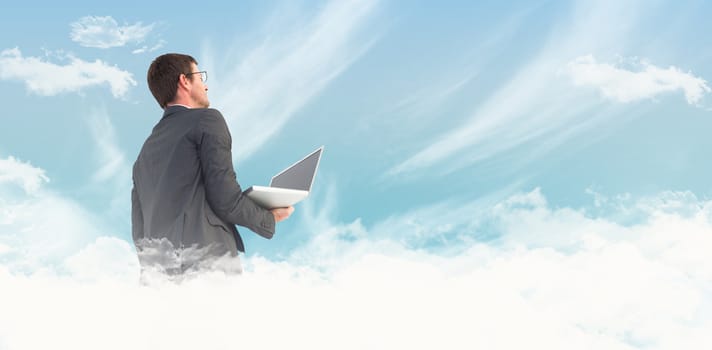 Businessman looking up holding laptop against blue sky