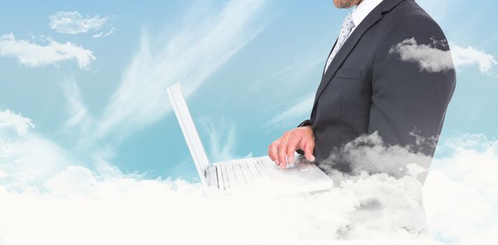Businessman holding laptop against blue sky