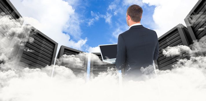 Businessman looking up holding laptop against blue sky with white clouds