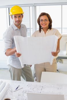 Portrait of two smiling young business people working on blueprints in the office