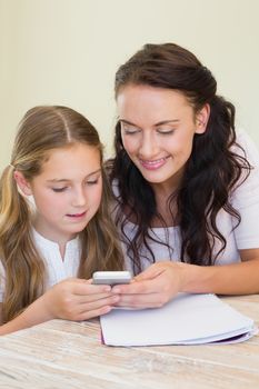 Mother and daughter using mobile phone together at table in house