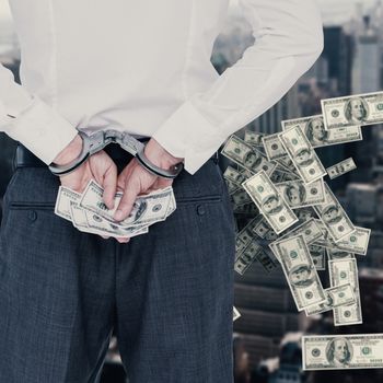 Businessman in handcuffs holding bribe against view of cityscape