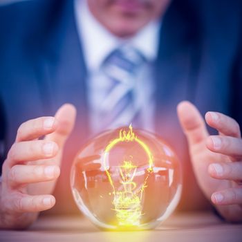 Bulb on fire on white background against businessman forecasting a crystal ball 