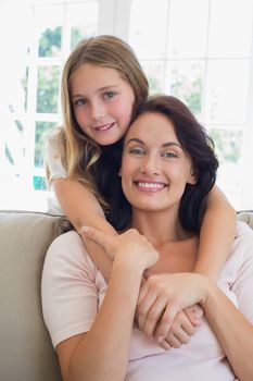 Portrait of little girl embracing mother from behind at home
