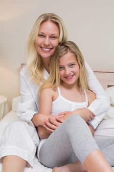 Portrait of loving mother and daughter sitting in bed at home