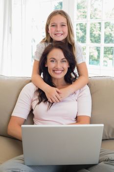 Portrait of little girl with mother using laptop on sofa at home