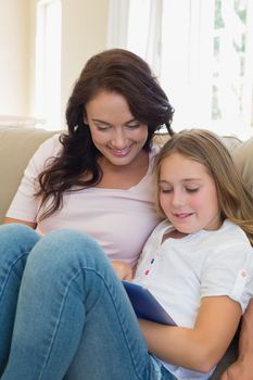 Young woman and daughter using tablet computer on sofa at home