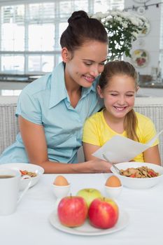 Happy mother and daughter reading greeting card at breakfast table