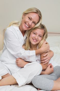 Portrait of happy mother hugging cute daughter in bed at home