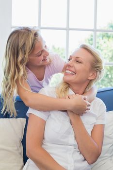 Happy mother looking at daughter embracing her from behind in living room