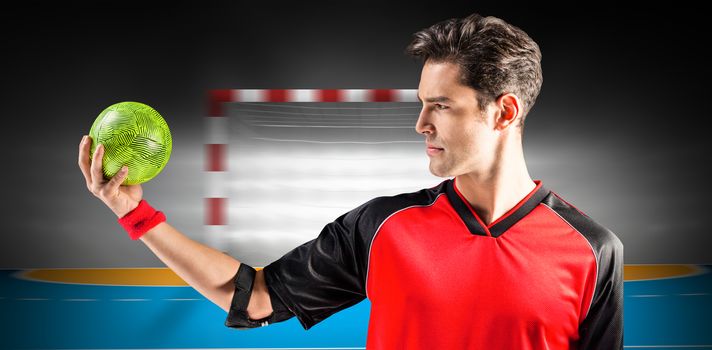 Confident athlete man holding a ball  against handball field indoor 