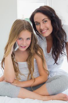 Portrait of little girl using mobile phone while sitting with mother in bed at home