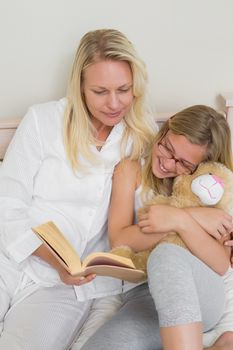 High angle view of happy mother and daughter reading story book in bed at home
