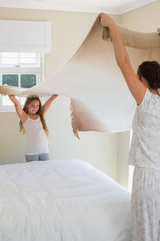 Mother and daughter making bed together in house