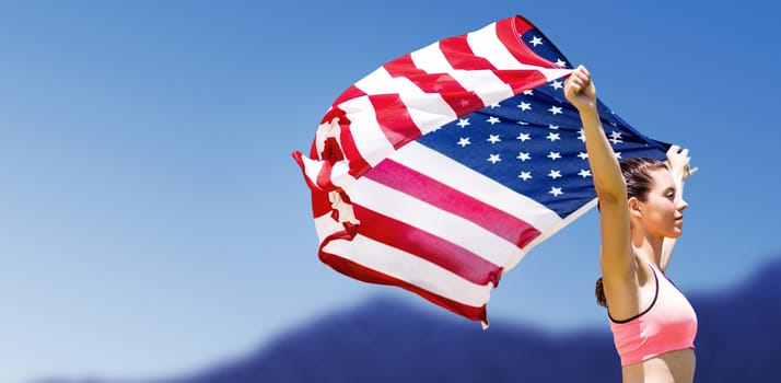 Profile view of sportswoman raising an american flag against scenic view of blue sky