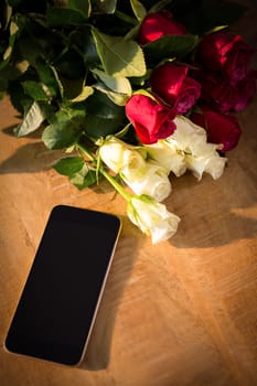 Close-up of yellow and red roses with smartphone on the wooden table