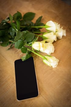 Close-up of yellow roses and smartphone on the wooden table