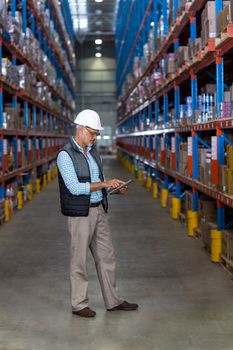 View of worker is using a tablet in front of shelves in a warehouse