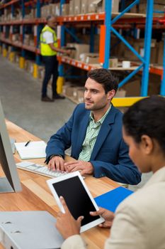 Focus on manager is working on a computer with his colleague in a warehouse