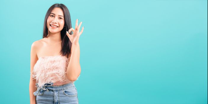 Smiling face asian beautiful woman her showing OK hand sign and looking to camera on blue background, with copy space for text