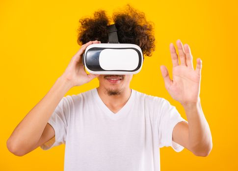 Asian handsome man with curly hair he using virtual reality headset or VR glass isolate on yellow background