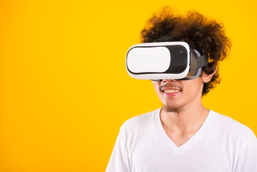 Asian handsome man with curly hair he using virtual reality headset or VR glass isolate on yellow background