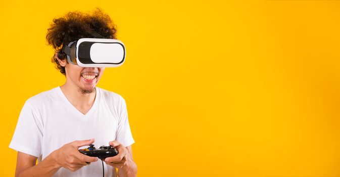 Asian handsome man with curly hair play game he using virtual reality headset or VR glass isolate on yellow background with copy space for text