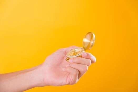 Hand holding antique brass compass isolated on yellow background with copy space for text