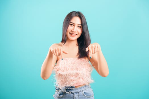 Smiling face asian beautiful woman her pointing finger down and looking to camera on blue background, with copy space for text