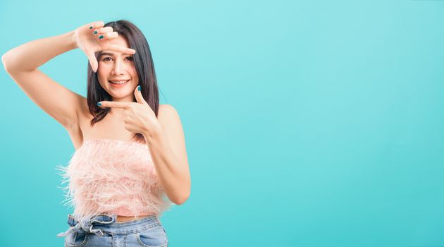 Smiling face asian beautiful woman her showing frame finger sign looking to camera on blue background, with copy space for text