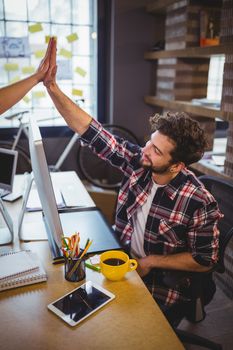 Creative business people high fiving at desk in office