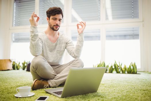 Young businessman doing yoga in front of laptop in creative office