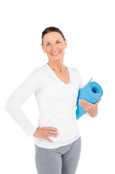 Portrait of smiling mature woman holding exercise mat while standing on white background