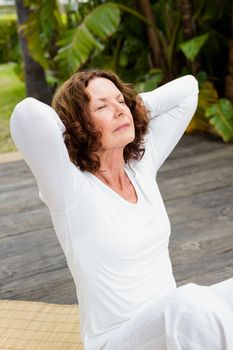 Mature woman with hands behind head while doing yoga