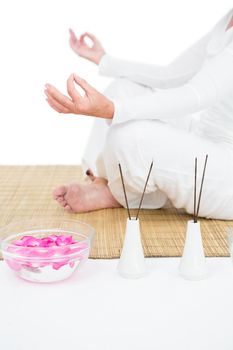 Low section of woman meditating against white background