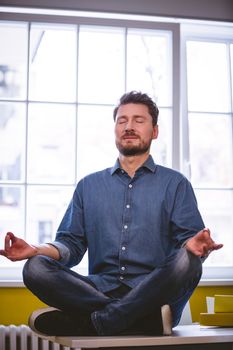 Young male executive meditating in lotus position at creative office