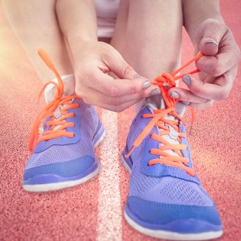 Portrait of athlete woman tying her running shoes against focus of race track 