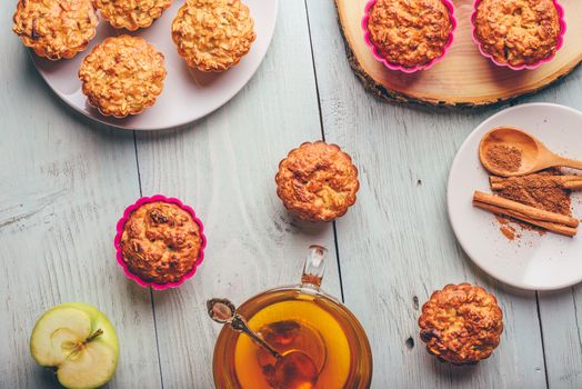 Healthy Breakfast. Cooked oatmeal muffins with apple and cup of green tea over light wooden background. View from above.